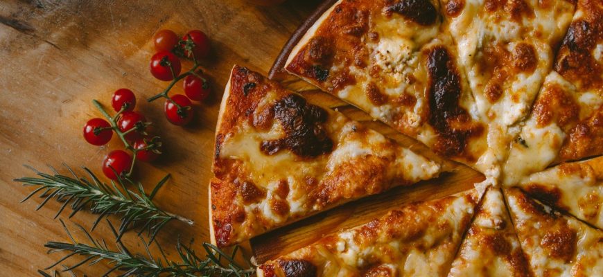 A sliced cheese pizza with cherry tomatoes and rosemary on a wooden board