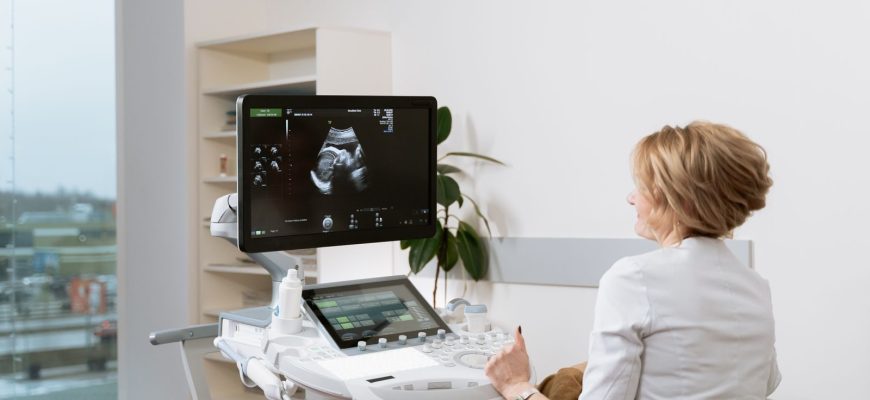 Doctor performing a prenatal ultrasound scan with medical equipment in a clinic.